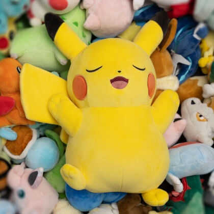Pikachu plush sleeping on top of more plushies.